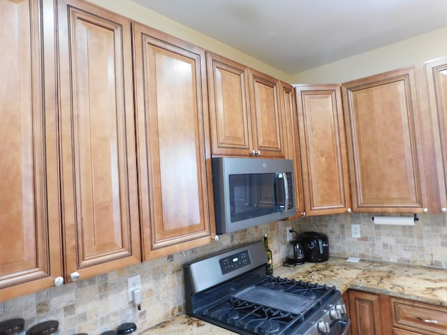 kitchen with tasteful backsplash, appliances with stainless steel finishes, and light stone counters