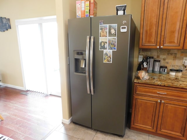 kitchen featuring stone counters, light tile patterned flooring, decorative backsplash, and stainless steel fridge with ice dispenser