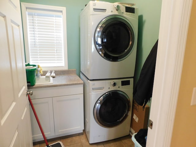 clothes washing area featuring light tile patterned flooring, cabinets, and stacked washing maching and dryer