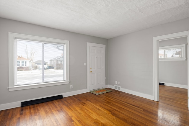 unfurnished room with dark wood-type flooring, a baseboard radiator, plenty of natural light, and a textured ceiling