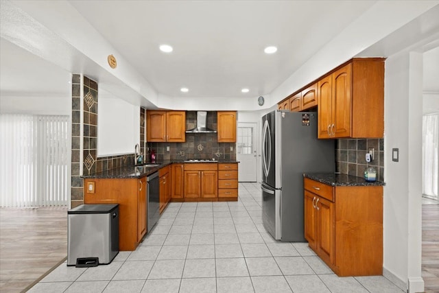 kitchen featuring wall chimney range hood, sink, dark stone countertops, black appliances, and decorative backsplash