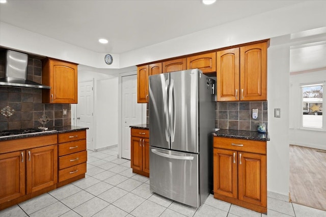 kitchen featuring stainless steel refrigerator, gas cooktop, wall chimney exhaust hood, and backsplash