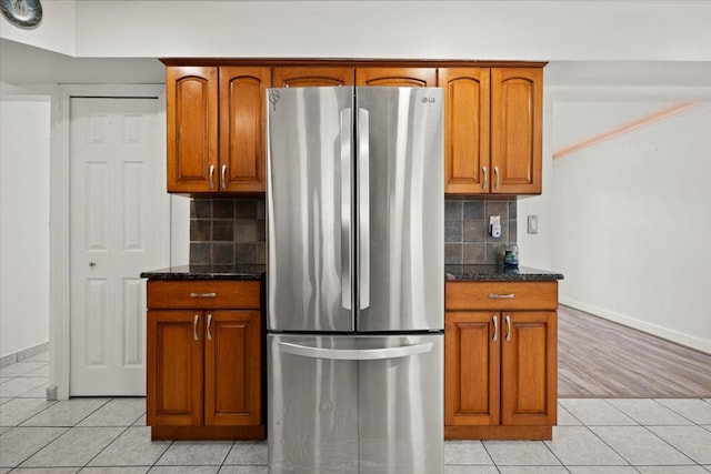 kitchen with stainless steel refrigerator, dark stone counters, light tile patterned flooring, and backsplash