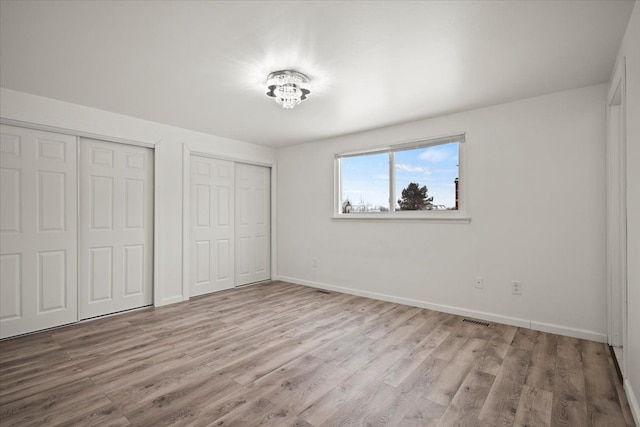 unfurnished bedroom featuring two closets and light hardwood / wood-style flooring