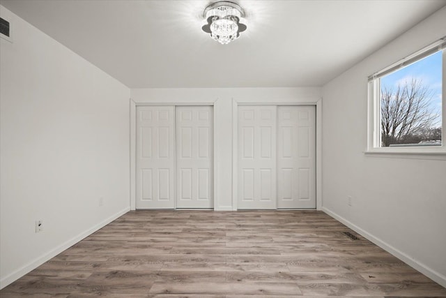 unfurnished bedroom featuring an inviting chandelier, two closets, and light hardwood / wood-style floors