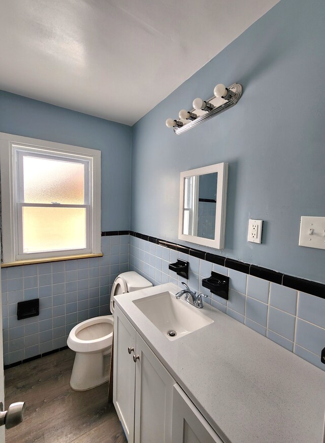 bathroom featuring tile walls, toilet, wood finished floors, vanity, and wainscoting