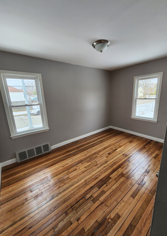 spare room featuring plenty of natural light, wood-type flooring, and baseboards