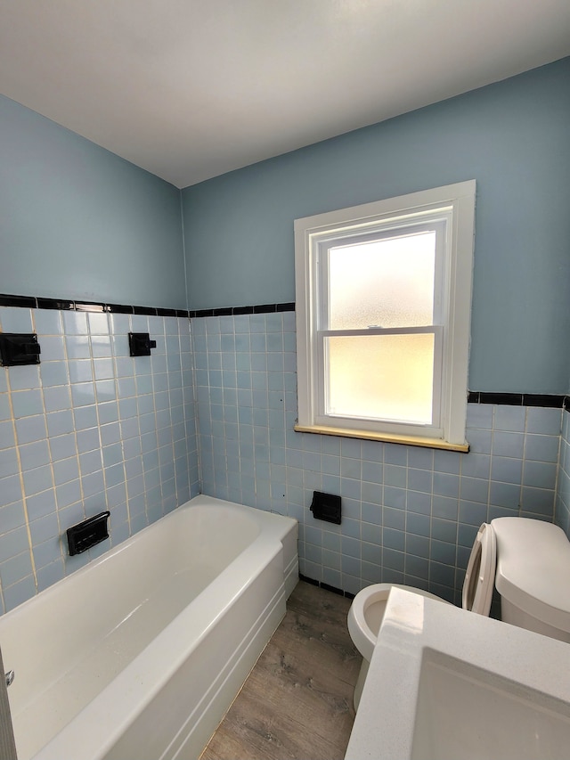 bathroom with hardwood / wood-style flooring, toilet, tile walls, and a washtub