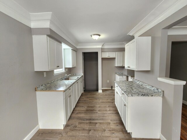 kitchen with a sink, baseboards, white cabinetry, wood finished floors, and ornamental molding