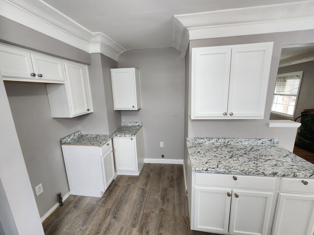 kitchen featuring dark wood-style flooring, white cabinetry, baseboards, crown molding, and light stone counters