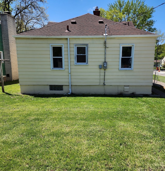 rear view of house featuring a yard, a chimney, and a shingled roof
