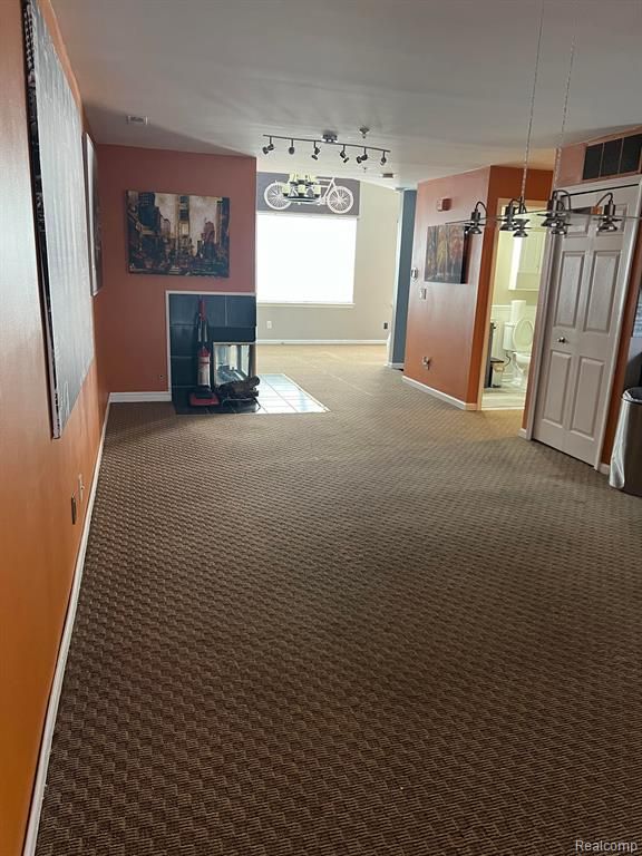 interior space with a tiled fireplace, rail lighting, and carpet flooring