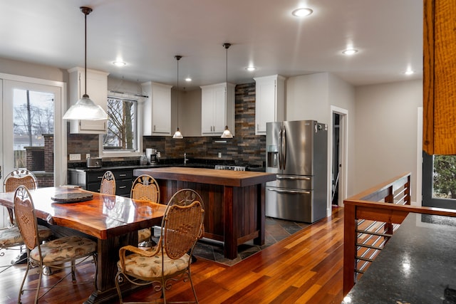 kitchen with white cabinets, decorative backsplash, hanging light fixtures, stainless steel fridge with ice dispenser, and dark wood-type flooring