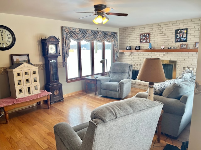 living room featuring a brick fireplace, light hardwood / wood-style floors, ceiling fan, and brick wall