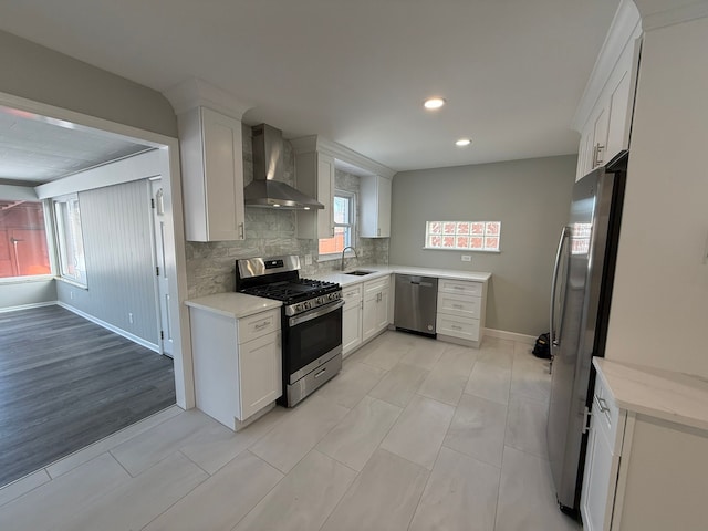 kitchen with appliances with stainless steel finishes, white cabinetry, sink, backsplash, and wall chimney exhaust hood