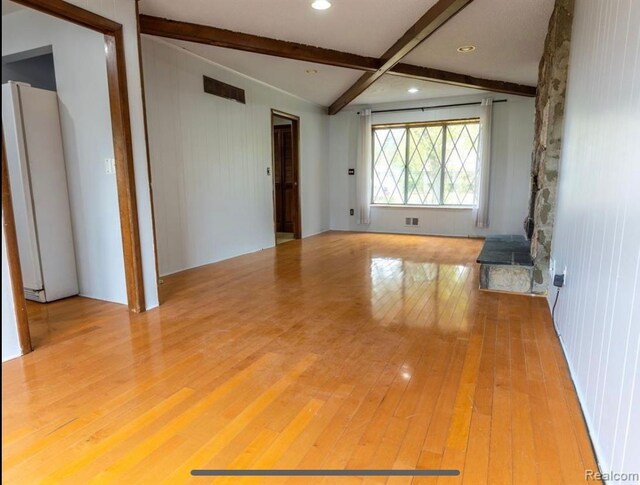 empty room with light hardwood / wood-style floors and vaulted ceiling with beams