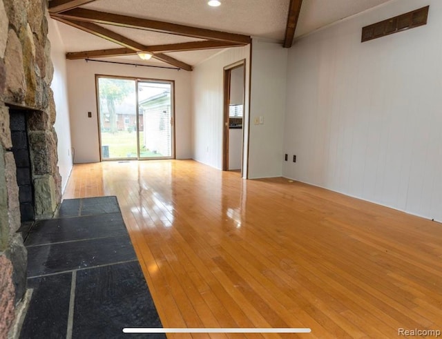 unfurnished living room featuring beamed ceiling, wood-type flooring, a fireplace, and a textured ceiling