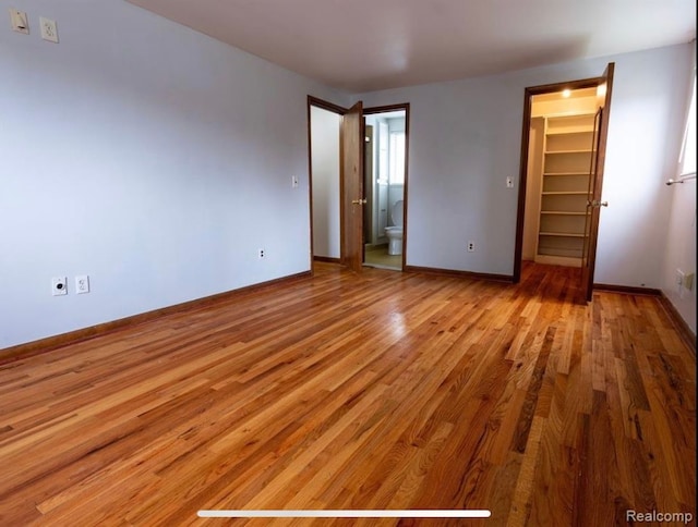 unfurnished bedroom featuring a walk in closet, a closet, and light hardwood / wood-style flooring