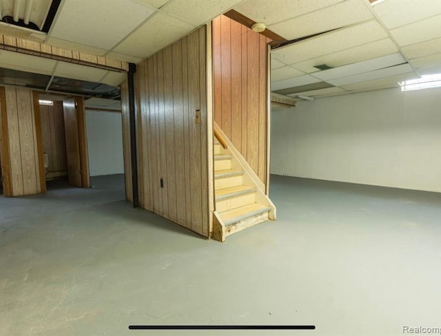 basement featuring a drop ceiling and wood walls