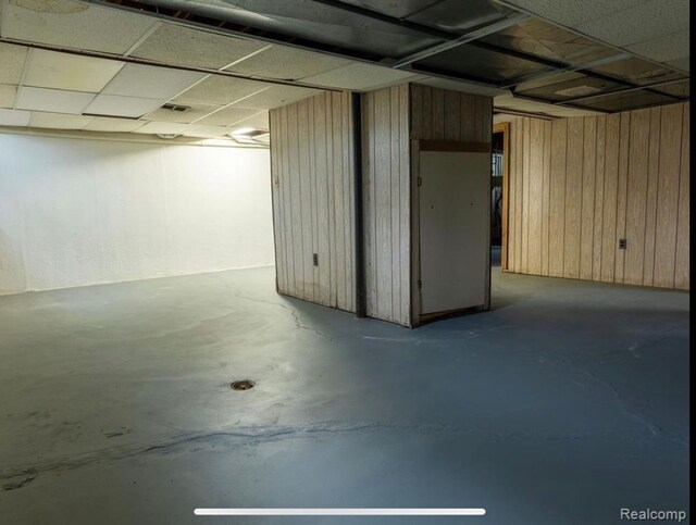 basement with a paneled ceiling and wooden walls