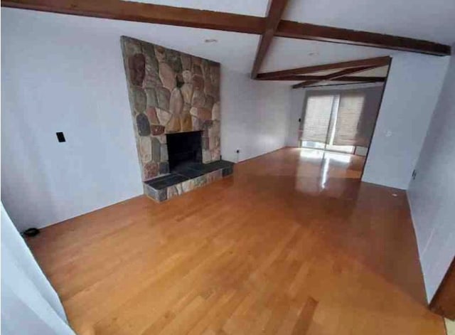 unfurnished living room featuring lofted ceiling with beams, a stone fireplace, and hardwood / wood-style floors