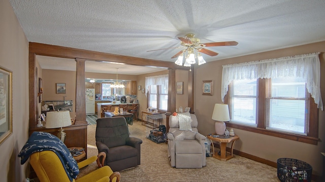 carpeted living room featuring ceiling fan with notable chandelier and decorative columns