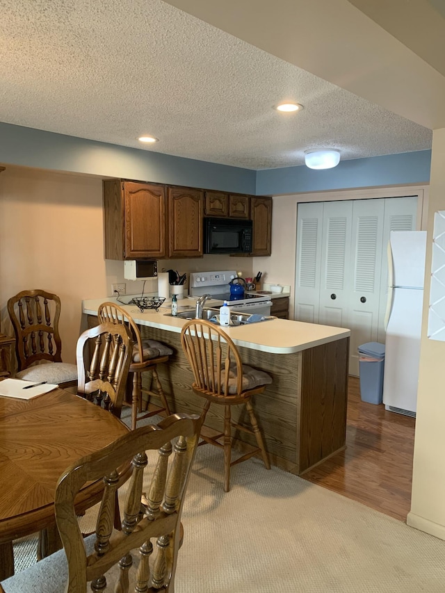 kitchen featuring white appliances, a breakfast bar area, a textured ceiling, kitchen peninsula, and light wood-type flooring