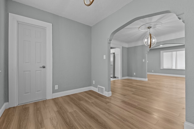 spare room featuring a notable chandelier and light wood-type flooring