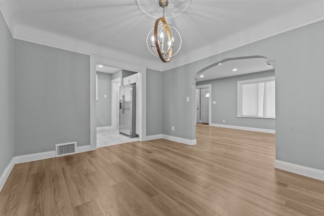 spare room with an inviting chandelier, a textured ceiling, and light wood-type flooring