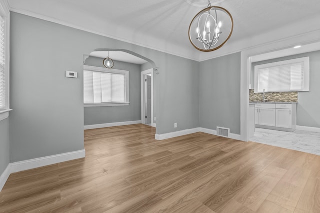 unfurnished dining area featuring ornamental molding, sink, light hardwood / wood-style flooring, and a notable chandelier