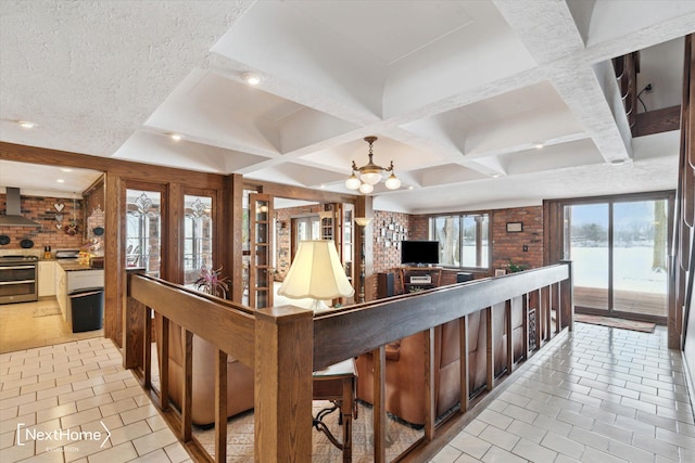 kitchen featuring a healthy amount of sunlight, wall chimney range hood, stainless steel stove, and an inviting chandelier