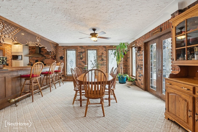 dining space featuring ceiling fan, a textured ceiling, brick wall, light colored carpet, and french doors