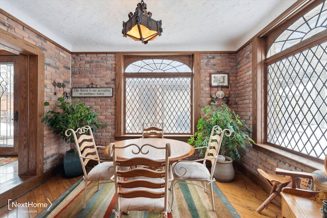 dining room featuring wood-type flooring, a textured ceiling, and brick wall