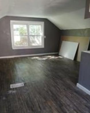 additional living space featuring dark wood-type flooring and vaulted ceiling