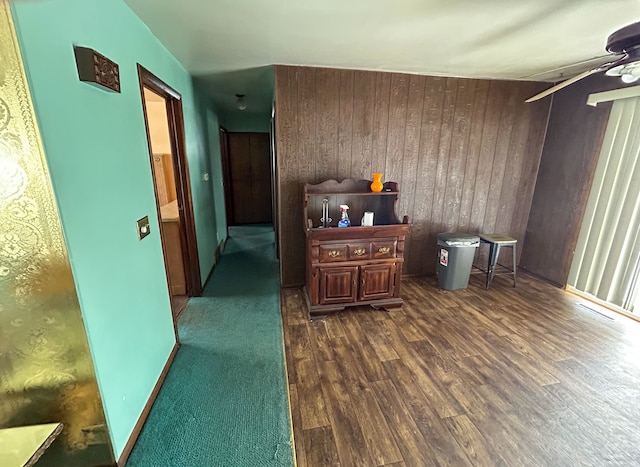 bar with dark wood-type flooring, ceiling fan, and wooden walls