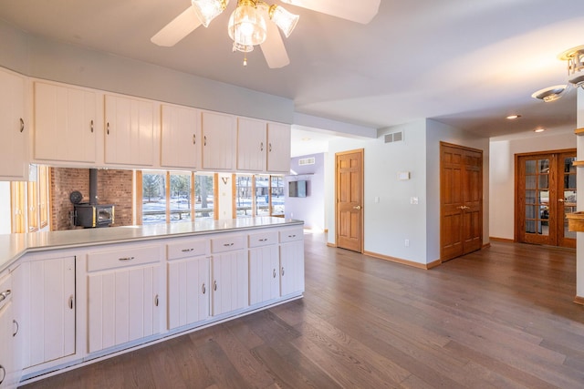 kitchen featuring white cabinetry, dark hardwood / wood-style floors, ceiling fan, and a wood stove