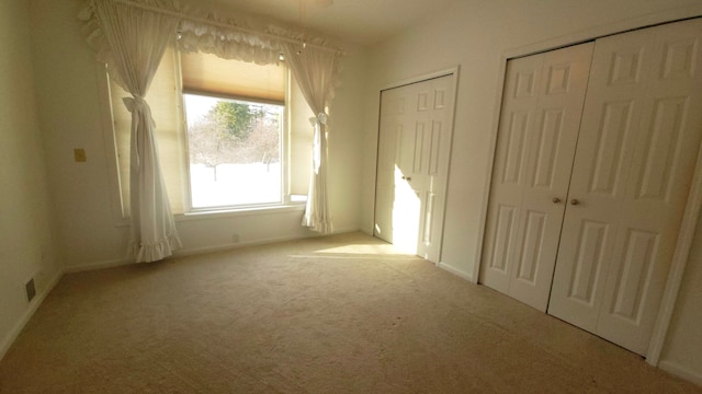 unfurnished bedroom featuring multiple closets and light colored carpet