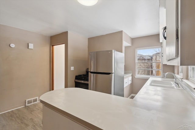 kitchen featuring sink, stainless steel refrigerator, black gas range, light hardwood / wood-style floors, and kitchen peninsula