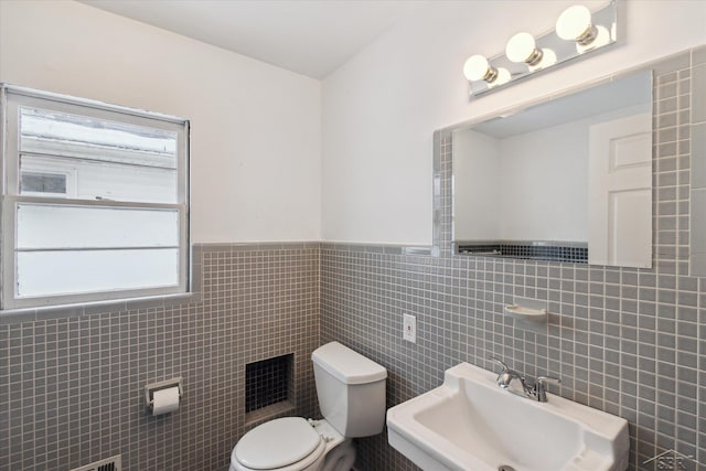 bathroom featuring toilet, sink, and tile walls