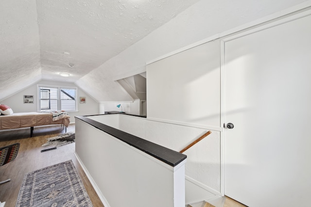 hallway featuring vaulted ceiling, hardwood / wood-style floors, and a textured ceiling