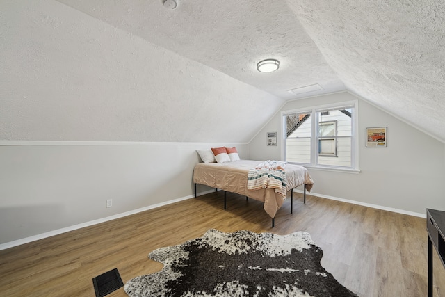 bedroom with lofted ceiling, wood-type flooring, and a textured ceiling