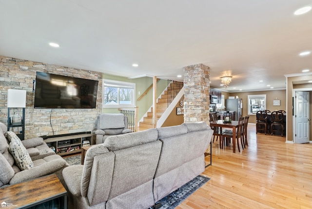 living room with decorative columns, ornamental molding, a stone fireplace, and light hardwood / wood-style flooring