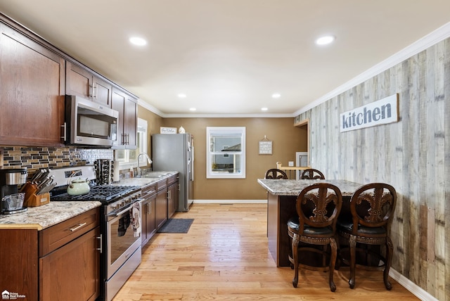 kitchen with sink, a kitchen breakfast bar, ornamental molding, stainless steel appliances, and light stone countertops