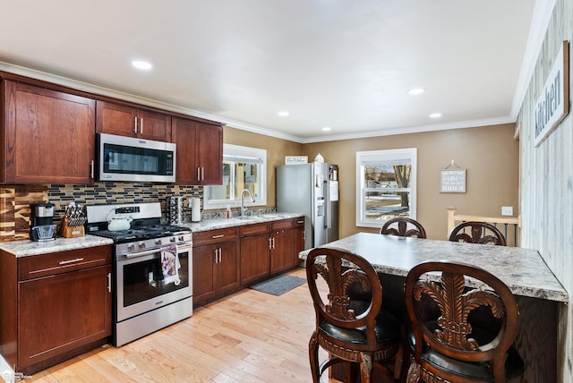 kitchen with sink, light stone counters, light hardwood / wood-style flooring, ornamental molding, and stainless steel appliances