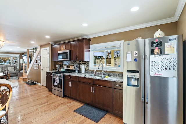 kitchen with sink, dark brown cabinets, light wood-type flooring, stainless steel appliances, and light stone countertops