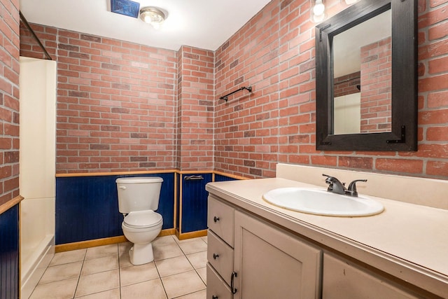 bathroom with tile patterned flooring, vanity, brick wall, and toilet