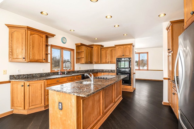 kitchen featuring sink, a center island with sink, dark hardwood / wood-style floors, dark stone counters, and black appliances