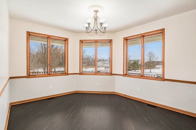 spare room featuring plenty of natural light, hardwood / wood-style floors, and a notable chandelier