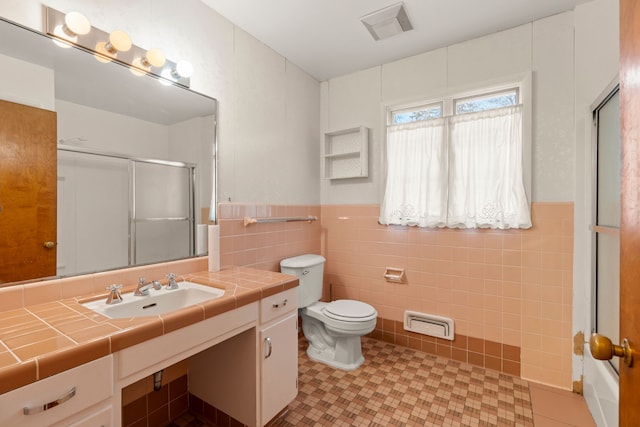 bathroom with tile walls, vanity, toilet, a shower with door, and tile patterned floors