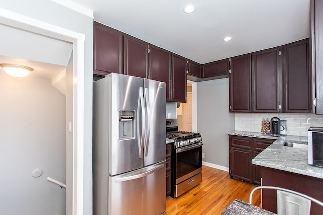 kitchen with light hardwood / wood-style flooring, backsplash, dark brown cabinets, stainless steel appliances, and light stone counters